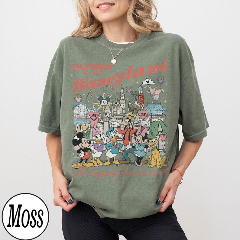 May include: Olive green t-shirt with a Disneyland graphic featuring Mickey Mouse, Minnie Mouse, Donald Duck, Goofy, and Pluto. The graphic includes the text "California Est. 1955 Disneyland" and "Where dreams come true."