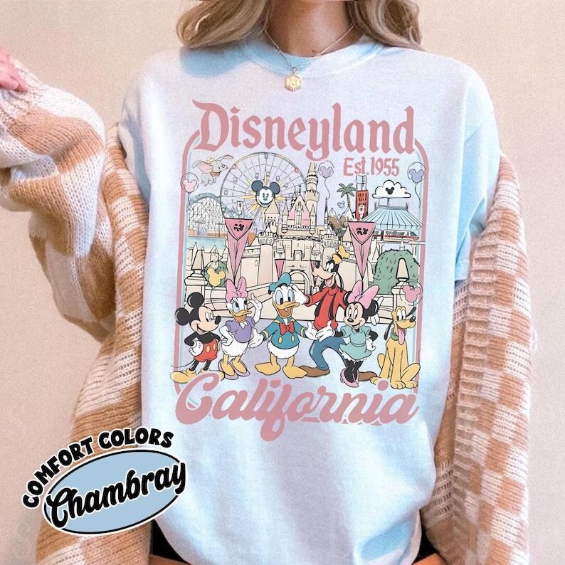 May include: Light blue Disneyland California sweatshirt with a graphic featuring Mickey Mouse, Minnie Mouse, Donald Duck, Daisy Duck, Goofy, and Pluto. The design includes the Disneyland castle, a Ferris wheel, and the text "Disneyland Est. 1955".
