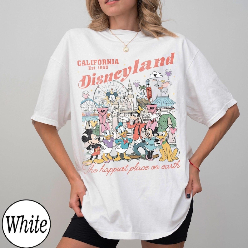 May include: White t-shirt with a Disneyland graphic. The design includes the text "California Disneyland Est. 1955" and "The happiest place on earth". The graphic features cartoon characters and park landmarks.