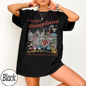 May include: Black t-shirt with a Disneyland graphic. The design includes the text "CALIFORNIA Est. 1955 Disneyland" and "The happiest place on earth" with cartoon characters and park imagery.