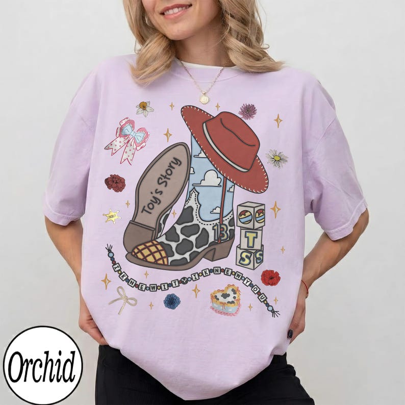Puede incluir: Una camiseta de color morado claro con un estampado gr&aacute;fico de una bota de vaquero con patr&oacute;n de vaca, un sombrero rojo y bloques con el texto Toy's Story. El dise&ntilde;o incluye un cord&oacute;n de cuentas con el texto I KNEW IT YOU KNEW IT YOU.