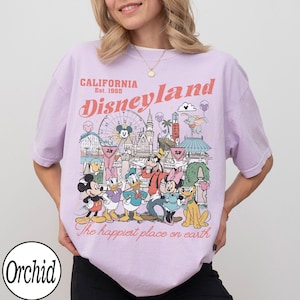 May include: A lilac t-shirt with a Disneyland graphic, including Mickey Mouse and friends. The design features the text "California Disneyland Est. 1955" and "The happiest place on earth."