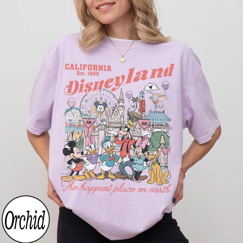 May include: A lilac t-shirt with a Disneyland graphic, including Mickey Mouse and friends. The design features the text "California Disneyland Est. 1955" and "The happiest place on earth."