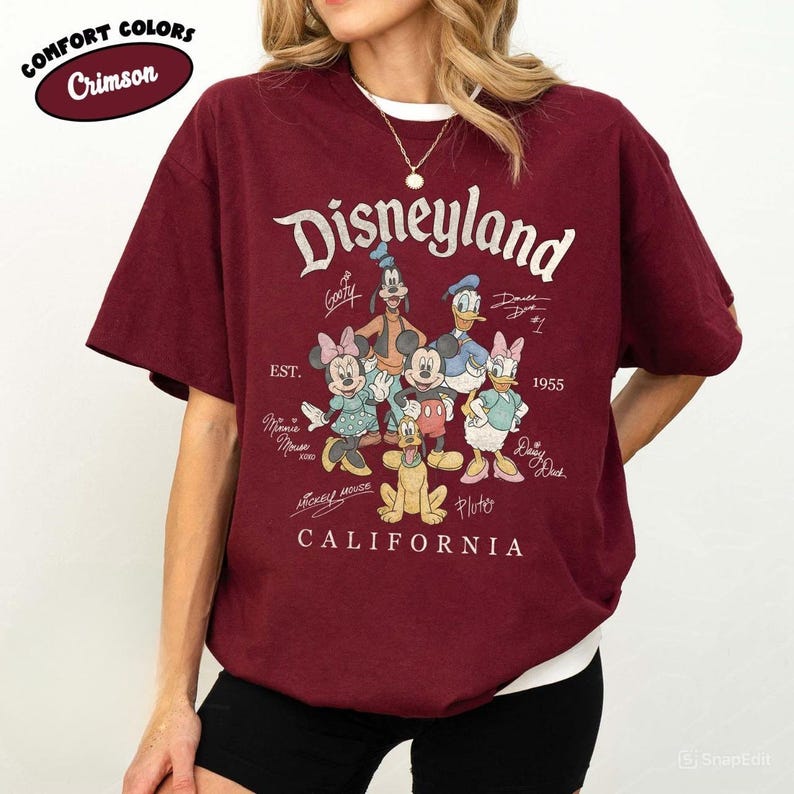 K&ouml;nnte beinhalten: Karmesinrotes T-Shirt mit wei&szlig;em Kragen und Disneyland-Grafik. Die Grafik zeigt das Disneyland-Logo, den Text "California" und Zeichentrickfiguren wie Mickey Mouse und Donald Duck. Das Shirt ist von der Marke Comfort Colors.