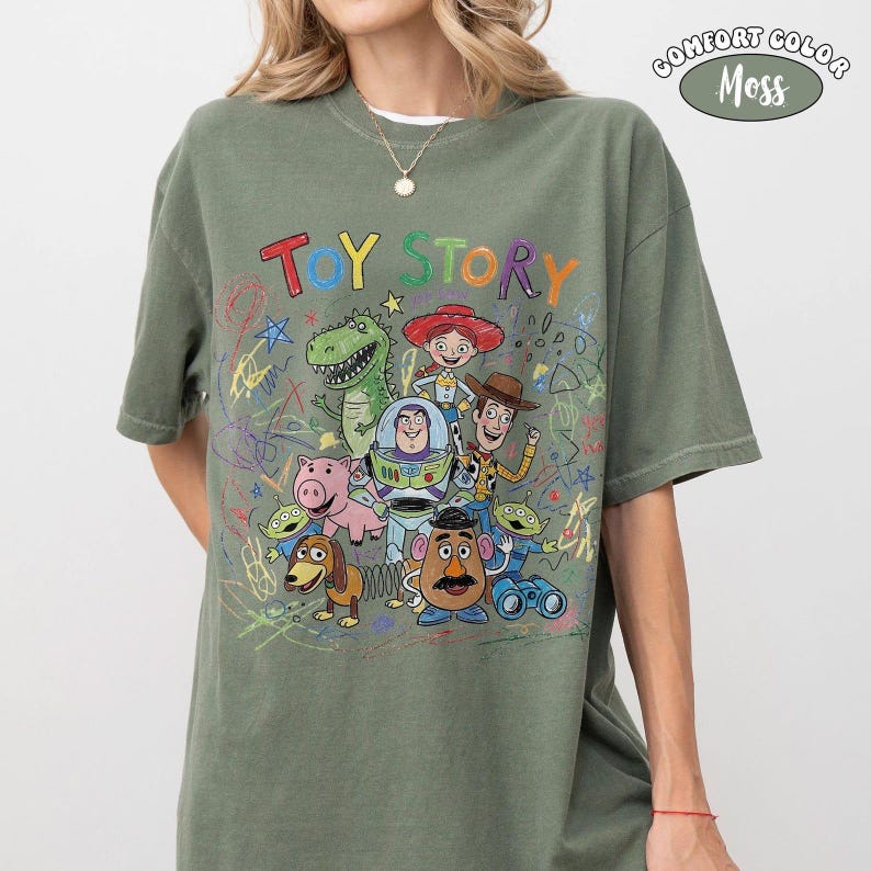 May include: A moss green t-shirt featuring a colorful graphic of Toy Story characters including Buzz Lightyear, Woody, Jessie, Rex, Hamm, Slinky Dog, Mr. Potato Head, and Aliens. The text TOY STORY is printed above the characters in multi-colored letters.