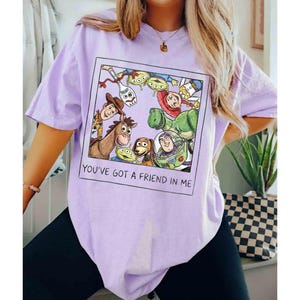 Puede incluir: Camiseta lila claro con un gr&aacute;fico enmarcado de personajes de Toy Story, incluyendo a Woody y Buzz Lightyear. El gr&aacute;fico est&aacute; rodeado de otros personajes de la pel&iacute;cula. El texto "YOU'VE GOT A FRIEND IN ME" est&aacute; debajo.