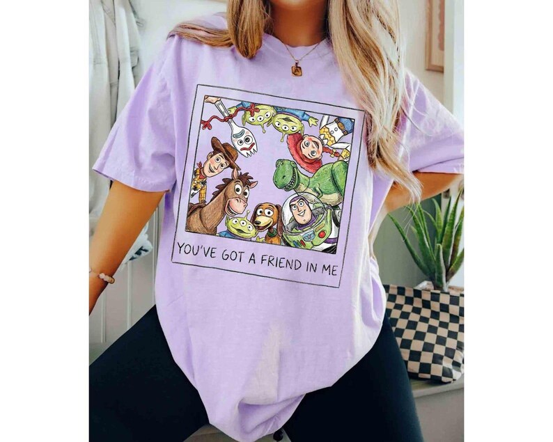 Puede incluir: Camiseta lila claro con un gr&aacute;fico enmarcado de personajes de Toy Story, incluyendo a Woody y Buzz Lightyear. El gr&aacute;fico est&aacute; rodeado de otros personajes de la pel&iacute;cula. El texto "YOU'VE GOT A FRIEND IN ME" est&aacute; debajo.