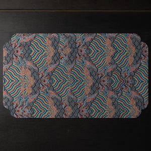 May include: Rectangular placemat with a repeating pattern of stylized paisley and wavy lines in shades of teal, orange, yellow, and blue. The edges have a rounded shape. The background is dark.