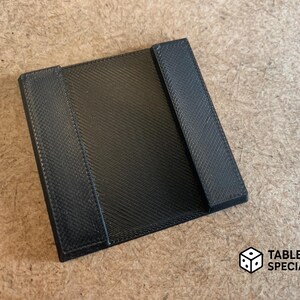 May include: A black, rectangular tabletop accessory with two raised side supports. The surface has a textured pattern. The logo "TABLETOP SPECIALIST" is visible in the lower right corner.