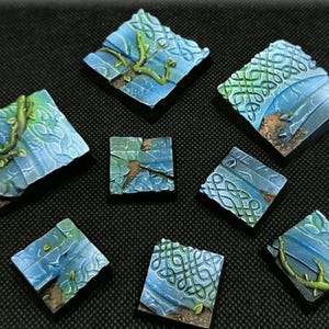 Op de afbeelding: Miniatuur terreinbases in blauw en groen. De bases hebben een steenachtige textuur met Keltische knoopmotieven en wijnranken. De bases zijn vierkant en van verschillende afmetingen, perfect voor tabletop games.