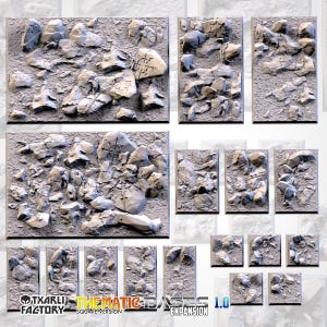 May include: A collection of gray, textured, square and rectangular bases with a rocky terrain design. Some bases feature engraved symbols. The bases are labeled "Thematic Bases 1.0 Expansion" and "Txarli Factory".