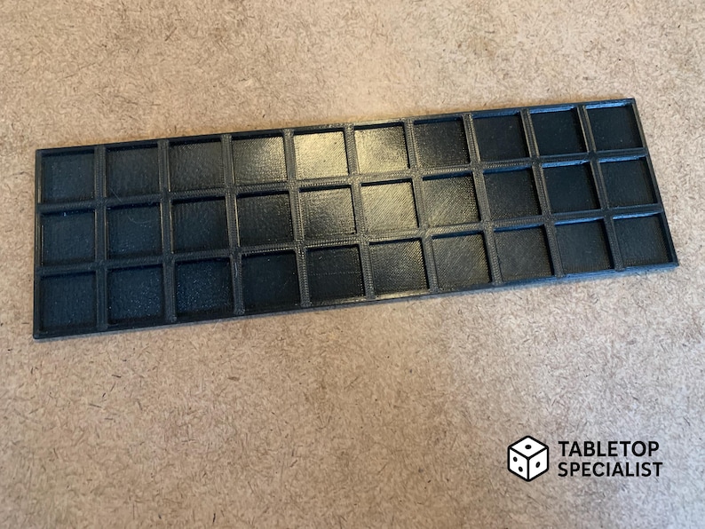 Op de afbeelding: Een zwart, rechthoekig dienblad met 30 vierkante vakken. De lade is gemaakt van een materiaal met textuur en is ontworpen om kleine items in te bewaren. Het Tabletop Specialist-logo staat rechtsonder.
