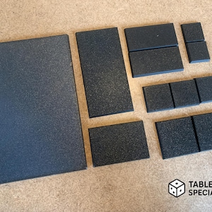 Könnte beinhalten: Eine Sammlung schwarzer, strukturierter Spielbrettfliesen in verschiedenen rechteckigen Formen. Das Set enthält ein großes Quadrat, mehrere Rechtecke und kleinere quadratische Teile. Das Zubehör für Tischspiele ist auf einer hellbraunen Oberfläche angeordnet.