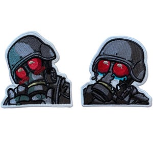 Könnte beinhalten: Zwei aufgestickte Aufnäher mit einem Cartoon-Soldaten mit Gasmaske und Helm. Der Soldat hat rote Augen und weint. Die Aufnäher sind grau, schwarz und weiß, mit einer blauen Umrandung.