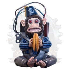 Könnte beinhalten: Skurrile Affenfigur mit Fez-Hut und zwei goldenen Gegenständen. Der Affe hat rote Augen und trägt ein blau-graues Outfit. Drähte und ein Zahnrad sind hinter dem Affen zu sehen. Der Text "THE TOP" befindet sich unten.