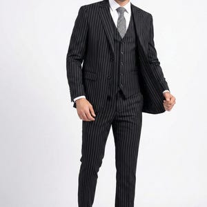 Puede incluir: Un traje de tres piezas a rayas negras con camisa blanca y corbata estampada. El traje incluye chaqueta, chaleco y pantalón. También se ven zapatos negros. El texto "THA Fashion Tailor" es visible en la imagen.