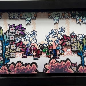 Könnte beinhalten: Ein gerahmtes 3D-Kunstwerk mit einer Szene mit mehreren bunten Yoshi-Charakteren im Pixelstil. Der Hintergrund umfasst stilisierte Blumen und Blätter in Rosa-, Blau- und Grüntönen, vor einem weißen und beigen Hintergrund.