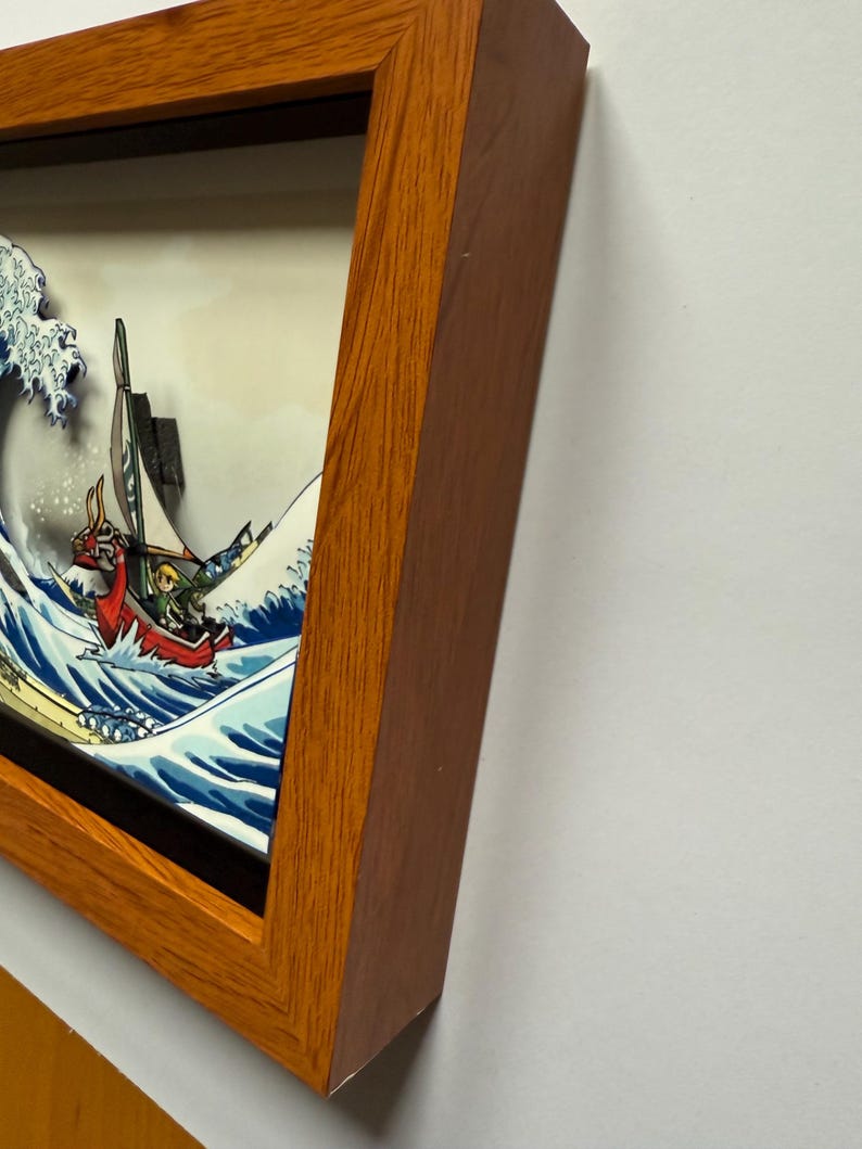 Pode incluir: Uma obra de arte emoldurada que retrata um barco estilizado navegando em uma grande onda, com um personagem no barco. A obra de arte est&aacute; em uma moldura de madeira. A onda &eacute; azul e branca, e o barco &eacute; vermelho.