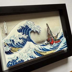 Pode incluir: Uma obra de arte 3D emoldurada que retrata uma onda oce&acirc;nica estilizada com barcos. A onda &eacute; renderizada em tons de azul e branco, com um barco em primeiro plano e dois outros ao fundo. A obra de arte &eacute; emoldurada em preto.