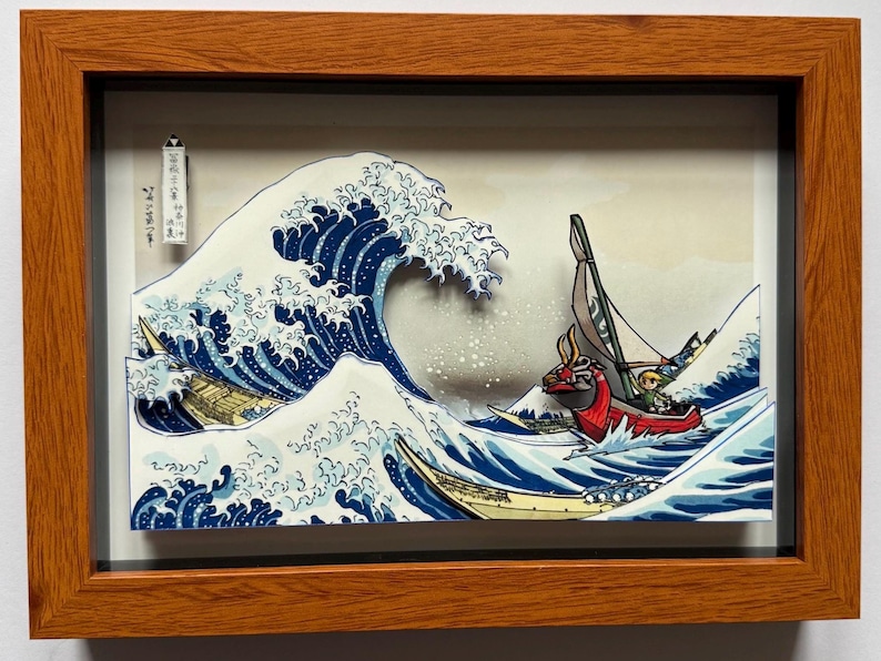 Pode incluir: Obra de arte 3D emoldurada retratando uma onda oce&acirc;nica estilizada com barcos, inspirada na arte japonesa. A onda &eacute; azul escuro com espuma branca, e os barcos s&atilde;o vermelhos e amarelos. A obra de arte est&aacute; em uma moldura de madeira.