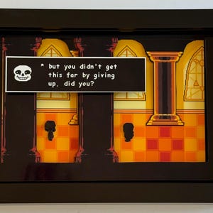 Op de afbeelding: Ingelijst kunstwerk met een scène uit een videogame. De afbeelding heeft een gepixelde achtergrond in geel en oranje, in een zwart frame. Een tekstballon bevat de tekst: "* but you didn't get this far by giving up, did you?"