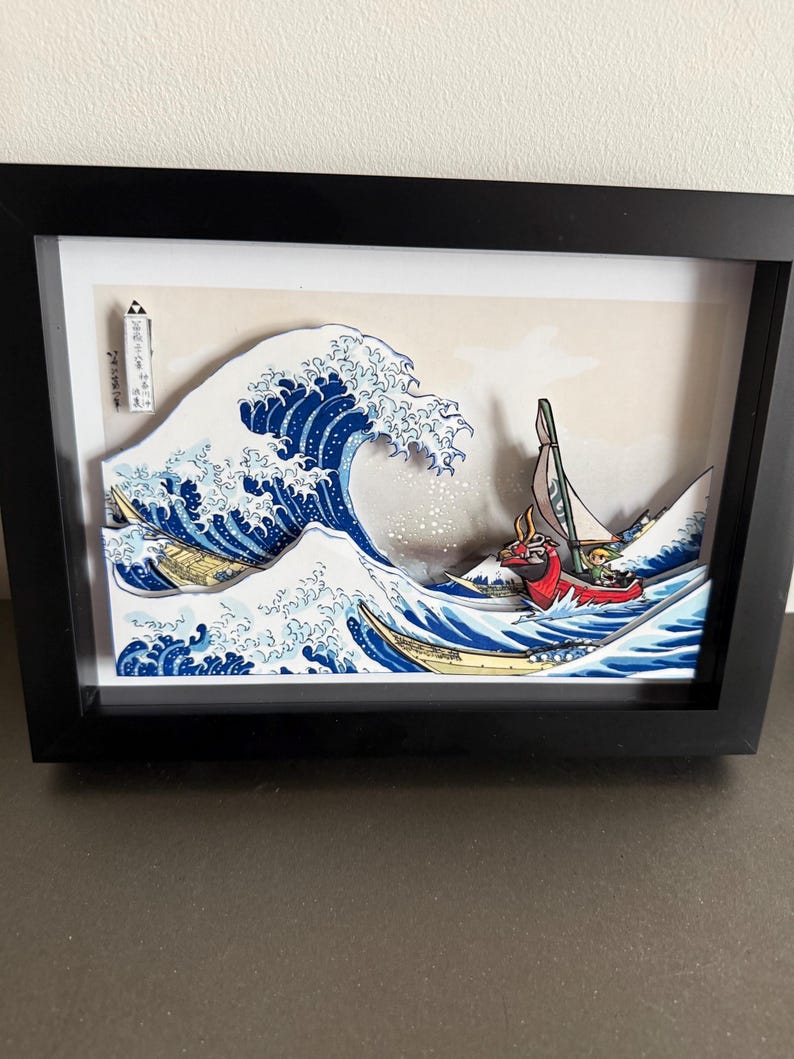 Pode incluir: Obra de arte 3D emoldurada que retrata uma onda oce&acirc;nica estilizada com um barco. A onda &eacute; renderizada em tons de azul e branco, com um barco vermelho e amarelo. A obra de arte est&aacute; em uma moldura preta.