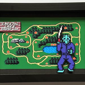 Op de afbeelding: Ingelijste pixelkunst met een kaart van Crystal Lake Camp en een gepixeleerde figuur met een machete. De kaart is groen met bruine wegen, bomen en hutten. De figuur draagt een blauwe overall en een masker. De lijst is zwart.