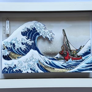 Pode incluir: Obra de arte emoldurada retratando uma cena oce&acirc;nica estilizada com uma grande onda azul e v&aacute;rios barcos. A obra apresenta um barco vermelho com um personagem e uma est&eacute;tica de estilo japon&ecirc;s. A moldura &eacute; branca.