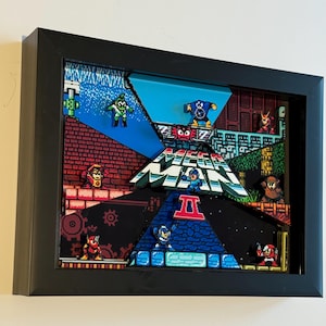 Könnte beinhalten: Gerahmtes 3D-Kunstwerk mit pixeligen Charakteren und Szenen aus dem Videospiel Mega Man. Das Kunstwerk hat einen schwarzen Rahmen und zeigt ein mehrschichtiges Design mit leuchtenden Farben wie Blau, Rot und Grün, wodurch eine dynamische und nostalgische Ästhetik entsteht.