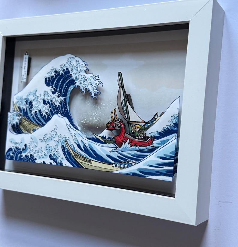 Pode incluir: Obra de arte emoldurada retratando uma cena de ondas estilizada com um barco. O barco apresenta uma figura de proa de drag&atilde;o vermelho e um personagem com uma t&uacute;nica verde. A obra de arte est&aacute; em uma moldura branca com uma borda preta.