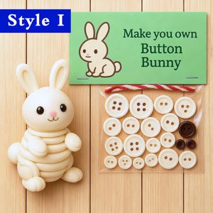 Puede incluir: Un conejito de botones blanco ensamblado se encuentra junto a una bolsa transparente de botones. La bolsa contiene botones blancos y marrones de varios tamaños. Una tarjeta verde con una ilustración de conejo y el texto "Make you own Button Bunny" está arriba.