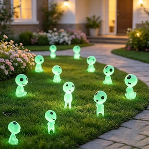 Puede incluir: Una colección de pequeñas figuras de color verde claro brillante con cabezas grandes y redondas y ojos circulares negros. Estos adornos de jardín lisos con forma humanoide están esparcidos por el césped y emiten una luz suave.