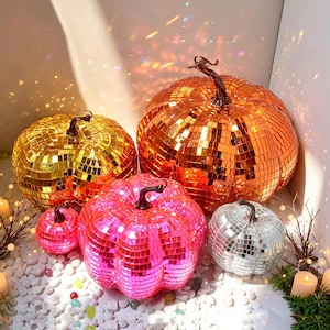 Op de afbeelding: Een set van vier pompoenvormige ornamenten bedekt met reflecterende spiegeltegels. De set bevat een grote oranje pompoen, een gouden, een roze en een kleine zilveren pompoen, elk voorzien van een donkerbruine steel.