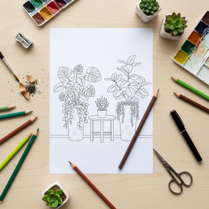 Op de afbeelding: Een bovenaanzicht van een kleurplaat met potplanten, omringd door kunstbenodigdheden. Kleurpotloden, aquarelverf, een penseel, een puntenslijper en kleine vetplanten zijn rond de pagina gerangschikt.