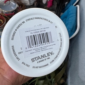 Puede incluir: Tapa blanca de vaso Stanley con c&oacute;digo de barras e informaci&oacute;n del producto. La tapa est&aacute; etiquetada como "Apto para lavavajillas" y "Sin BPA". El texto incluye "Dise&ntilde;ado en Seattle WA" y "No microondas".
