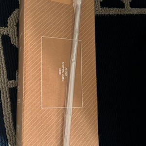 Puede incluir: Una caja de cart&oacute;n marr&oacute;n con rayas diagonales. La caja tiene una correa de pl&aacute;stico transparente y una etiqueta que dice "STANLEY". Se adjunta una etiqueta transparente con el texto "ATTACH SHIPPING LABEL HERE."