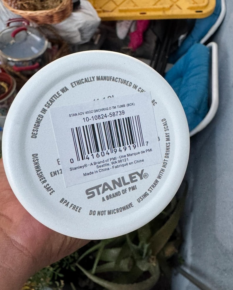 Puede incluir: Tapa blanca de vaso Stanley con c&oacute;digo de barras e informaci&oacute;n del producto. La tapa est&aacute; etiquetada como "Apto para lavavajillas" y "Sin BPA". El texto incluye "Dise&ntilde;ado en Seattle WA" y "No microondas".