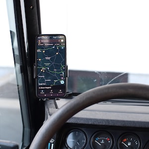 Könnte beinhalten: Ein Smartphone mit einer Kartenanwendung ist auf dem Armaturenbrett eines Autos montiert. Das Telefon wird in einer schwarzen Telefonhalterung gehalten. Das Armaturenbrett und das Lenkrad sind sichtbar, mit Anzeigen und dem Text "In dieser Gegend" auf dem Bildschirm.