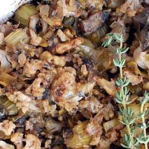 May include: Close-up of a baked dish with a mix of ingredients, including cauliflower, celery, and herbs. The dish is in a white ceramic baking dish. The food has a golden-brown color, indicating it has been baked.