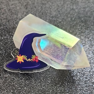 Puede incluir: Un sombrero de bruja morado con flores amarillas y rojas sobre un cristal transparente iridiscente.