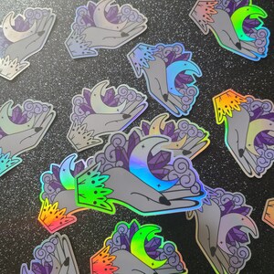 Puede incluir: Un conjunto de 10 pegatinas hologr&aacute;ficas iridiscentes con una mano sosteniendo una luna creciente y cristales. Las pegatinas son perfectas para agregar un toque de magia a tus diarios, port&aacute;tiles, botellas de agua y m&aacute;s.