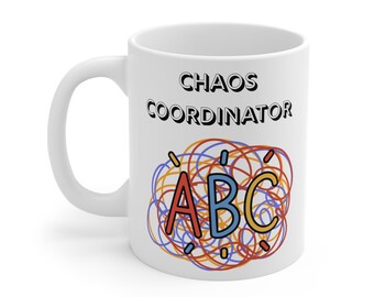 以下が含まれることがあります： 白いセラミックマグカップ。黒字で「CHAOS COORDINATOR」と書かれています。その下に、渦巻く線と赤、青、黄色の「ABC」の文字を使ったカラフルなデザインがあります。