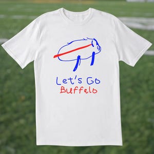 May include: White t-shirt featuring a blue and red graphic of a buffalo with the text "Let's Go Buffalo" in blue and red. The shirt is made of a soft material and is suitable for casual wear.
