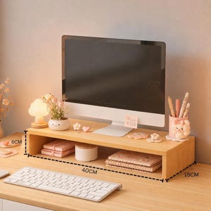 May include: A wooden monitor stand with a computer monitor on top. The stand is 18 inches wide and 40 inches long. The stand holds a lamp, a small plant, and other desk accessories. A keyboard is in front of the stand.