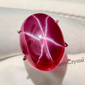 Peut inclure: Une pierre précieuse rubis ovale et vibrante, avec un effet d'étoile à six rayons. La pierre polie est de couleur rouge profond avec un motif d'étoile blanc brillant. La pierre est sertie de quatre petites griffes.
