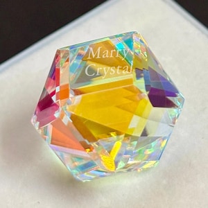 May include: A multi-faceted crystal gemstone with a rainbow iridescence, set in a white box. The crystal has a geometric shape and reflects various colors, including yellow, orange, and purple. The text "Marry Crystal" is visible on the crystal.