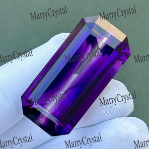 Può includere: Una pietra preziosa rettangolare sfaccettata con una tonalità viola intenso e una qualità trasparente. La pietra presenta bordi netti e puliti e una superficie lucida che riflette la luce, mostrando un colore viola vibrante in tutta la sua struttura.