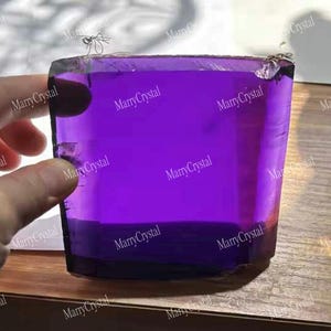 Può includere: Un esemplare di cristallo rettangolare, traslucido e di colore viola intenso, con superfici lisce e piatte e bordi netti e definiti. Il minerale presenta una tonalità viola vibrante e uniforme, che cattura la luce rivelando chiarezza interna.