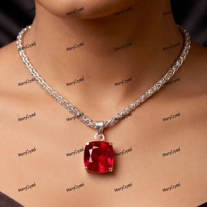 May include: A silver chain necklace featuring a large, square-cut, vibrant red gemstone pendant. The chain has a woven, textured link design, and the pendant is held by a simple silver bail, showcasing a faceted surface that reflects light.