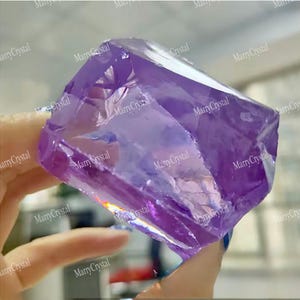 Puede incluir: Un espécimen de cristal de color púrpura intenso y translúcido con una forma geométrica facetada. La piedra muestra estructuras internas claras y bordes angulares afilados, reflejando la luz en sus superficies lisas y pulidas.